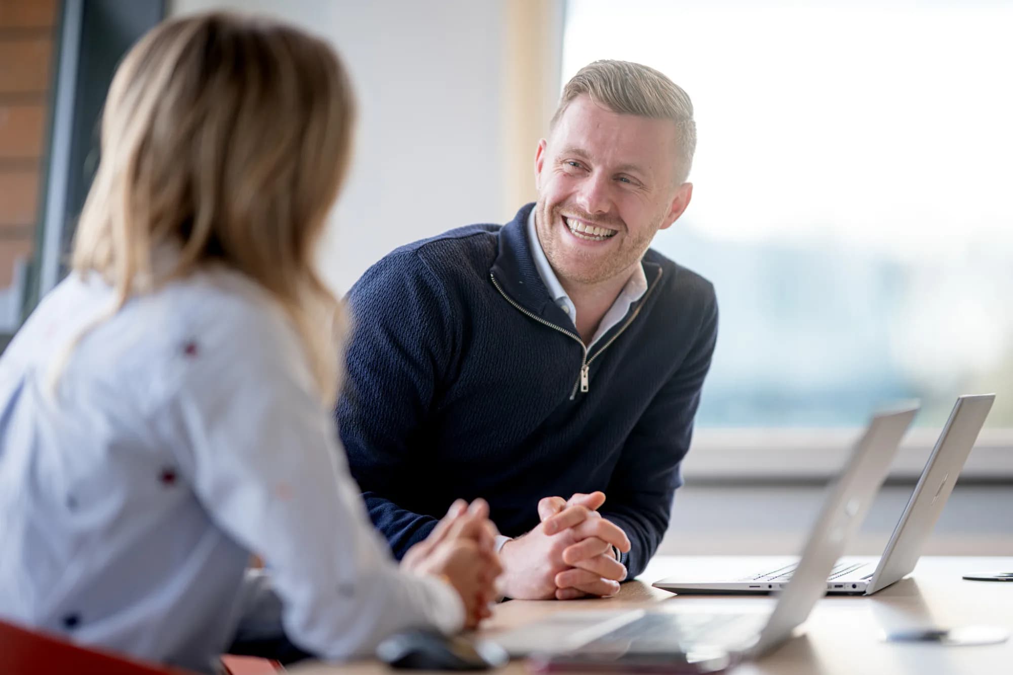 Twee collega's in gesprek aan een bureau met laptops